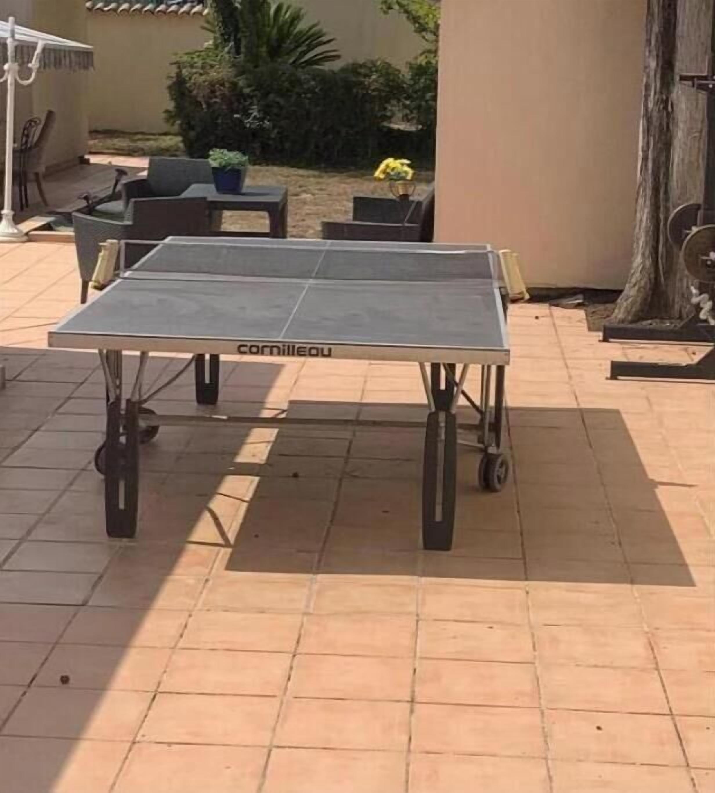 A portable ping pong table with wheels, labeled "cornilleau," on a tiled patio.