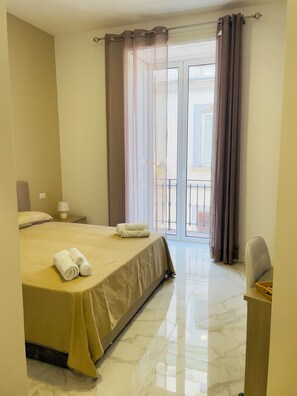 Una habitación de hotel con una cama, una mesita de noche, una lámpara, una silla y vistas al exterior.