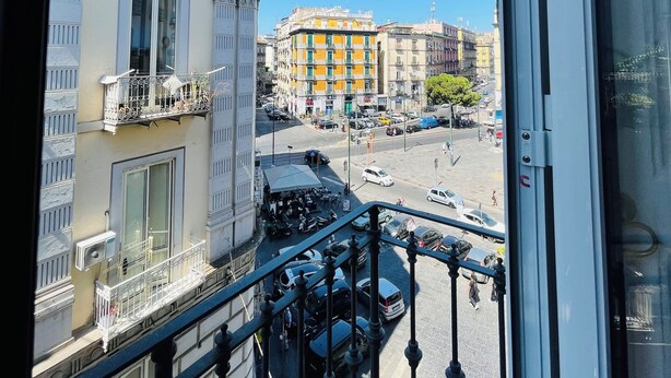A view from a balcony overlooking a street with buildings, cars, and a clear blue sky. - Nerisa Home (Napoli)