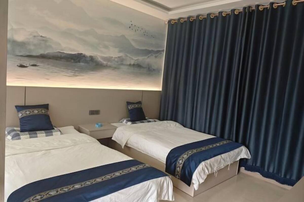 Hotellihuone, jossa on kaksi sänkyä, suuri seinämaalaus ja tummat verhot.