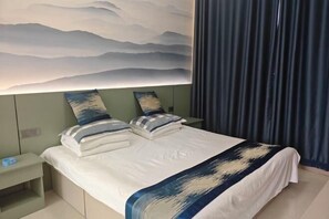 Una cama bien hecha con una colcha blanca y azul estampada, dos almohadas y una mesita de noche con una lámpara.