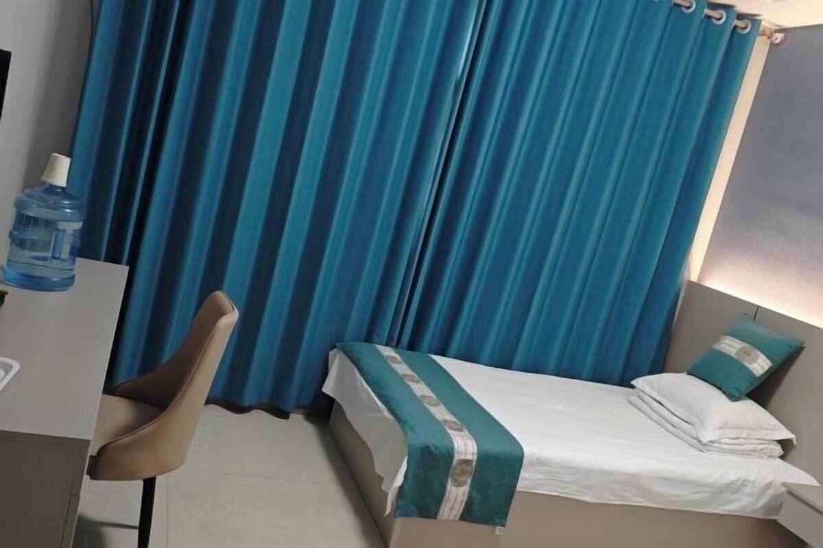 Hotellihuone, jossa on sänky, tuoli, vesipullo ja verhot.