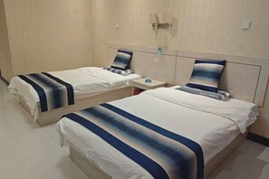 Dos camas individuales con cabeceras y mesitas de noche a juego, una lámpara de pared y una pequeña mesa entre ellas.