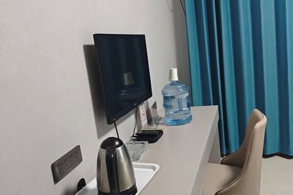 Habitación de hotel con televisor de pantalla plana montado en la pared, dispensador de agua, tetera, toma de corriente y una silla.