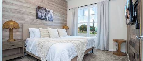 Un dormitorio con una cama grande, un televisor montado en la pared y un ventanal con cortinas.