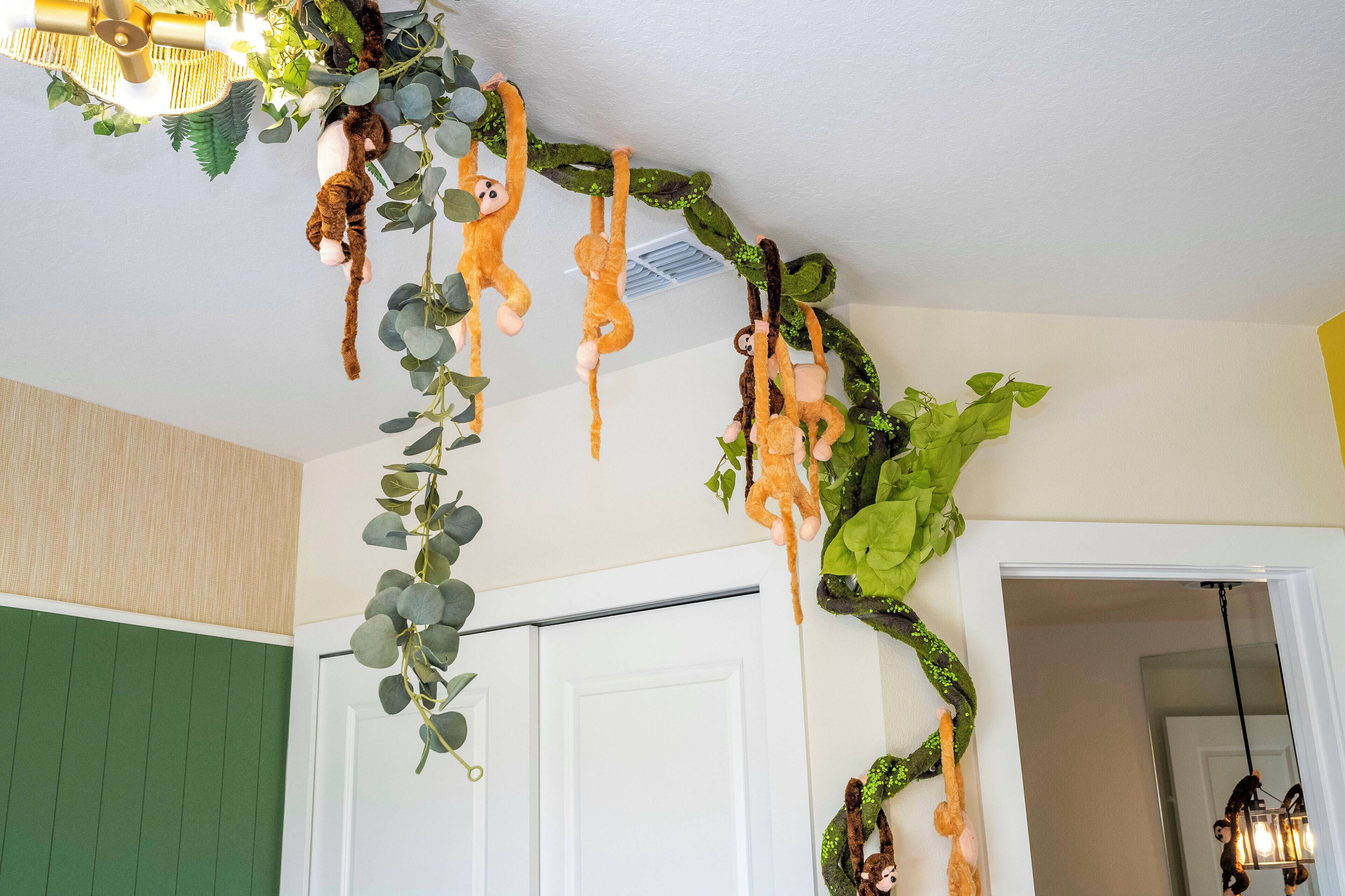 Ein Zimmer mit grüner Wand, einer weißen Tür und einer Decke mit hängenden Dekorationen, darunter Stofftiere und Pflanzen.