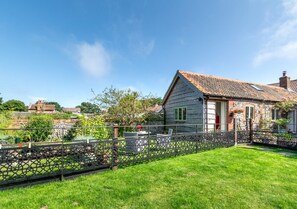 Situated in a lush, green setting, this charming house features a prominent red door and a decorative metal fence.