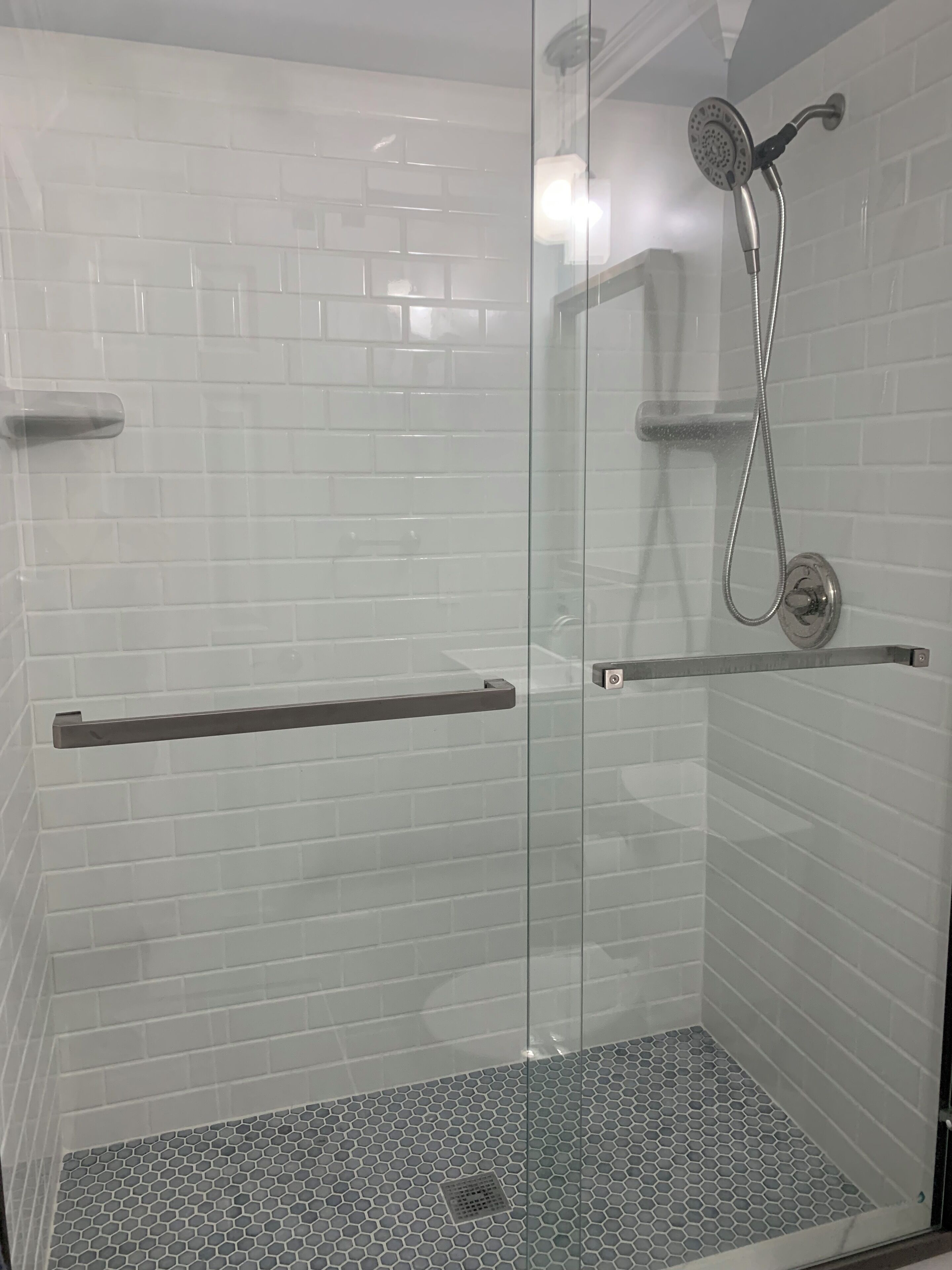 A glass-enclosed shower with white tiled walls and a hexagonal tile floor.