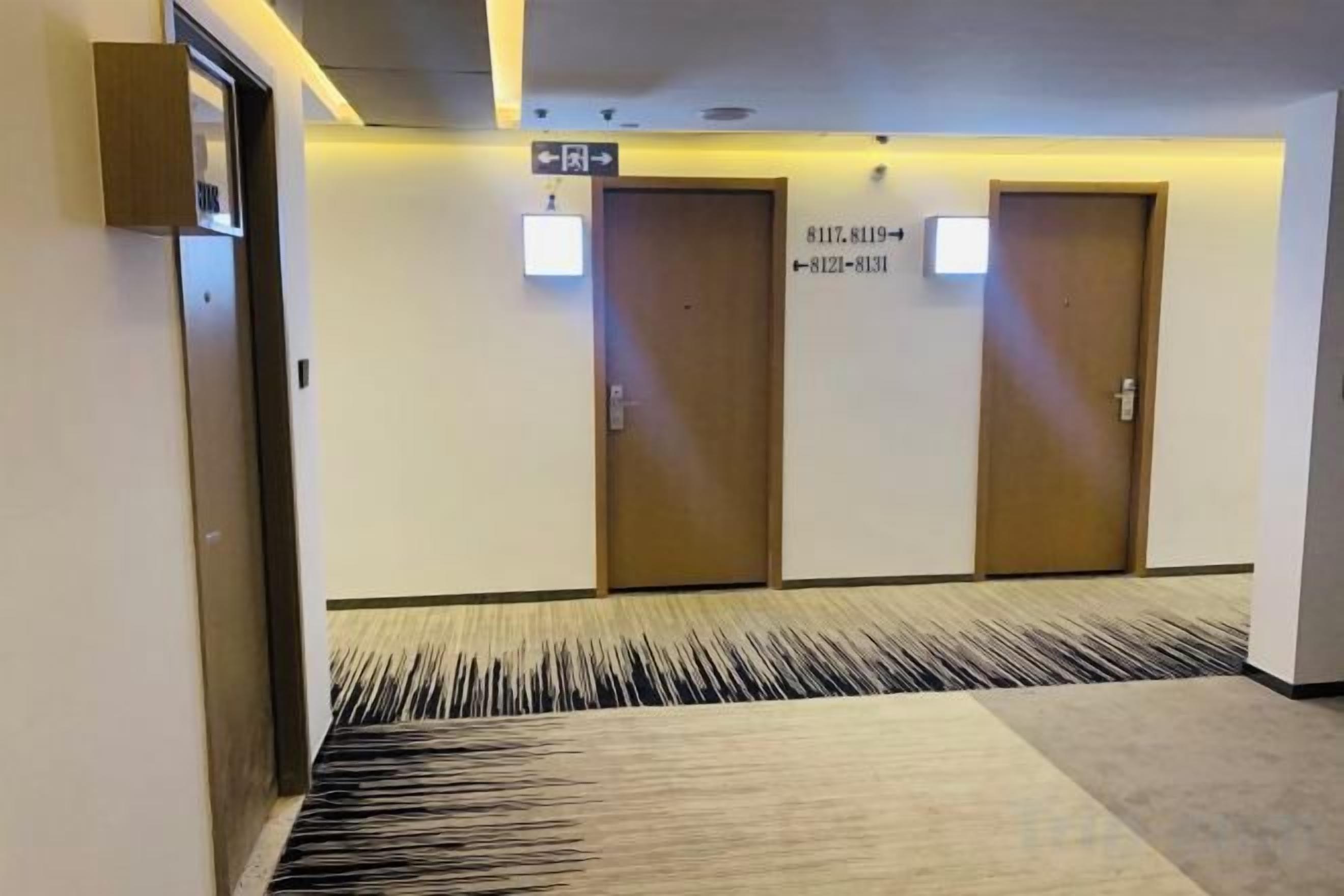 A hotel corridor with two doors, a patterned carpet, and a sign with room numbers.