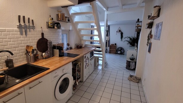Une cuisine compacte avec un lave-linge, un plan de travail en bois et des murs en briques blanches.