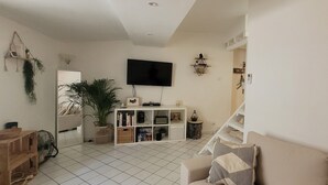 Un salon avec un canapé blanc, un téléviseur fixé au mur, une bibliothèque et un escalier menant à un autre niveau.