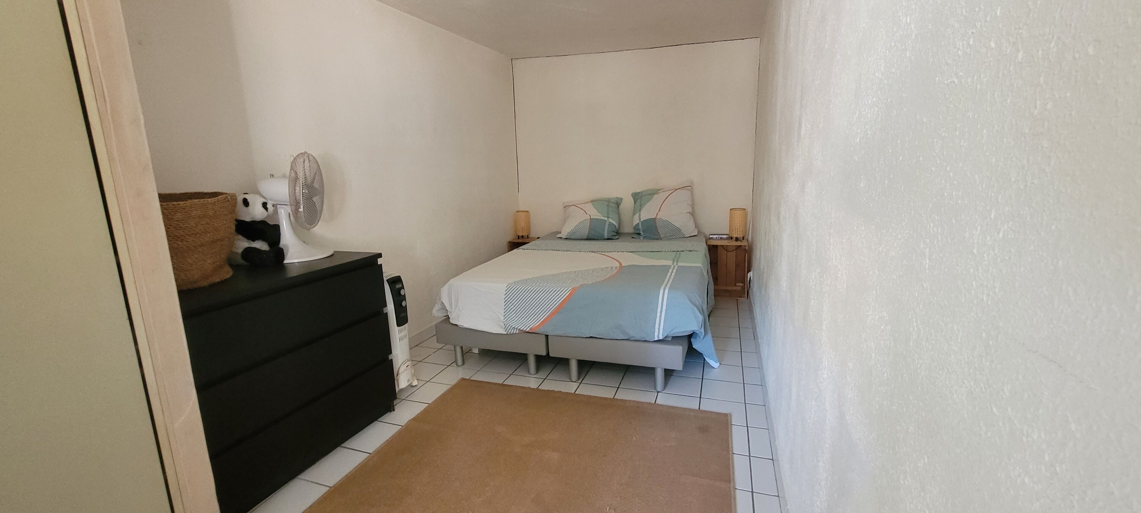 A bedroom with a bed, bedside lamps, a fan, and a dresser.