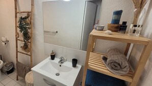 Une salle de bain équipée de toilettes, d’un lavabo, d’un miroir et d’étagères où sont rangés les articles de toilette.