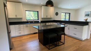 A modern kitchen with white cabinets, a large island, and a black countertop. - Escape to The Clyde’s View Hideaway in Manchester, Vt. New Home  3 Bed 2 Bath (Manchester Center)