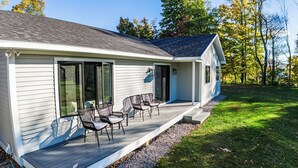 A single-story house with a covered porch, sliding glass doors, and a small deck area with outdoor furniture. - Escape to The Clyde’s View Hideaway in Manchester, Vt. New Home  3 Bed 2 Bath (Manchester Center)