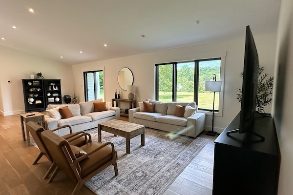 - Bright modern living room with large windows and mountain views - Two cozy sofas and stylish leather chairs for relaxation - Smart TV setup perfect for streaming your favorite shows