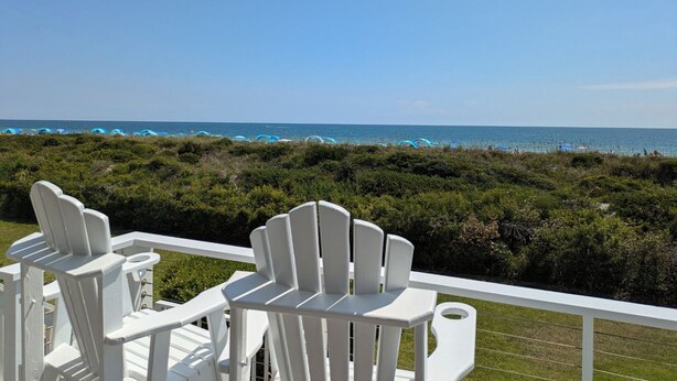 Eine Terrasse mit weißen Adirondack-Stühlen mit Blick auf einen Strand mit Zelten.