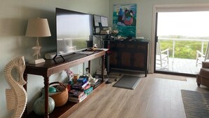 Ein Wohnzimmer mit Fernseher, Schreibtisch, Gemälde und Blick ins Freie.