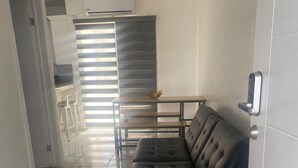 Un salón moderno con un sofá de cuero negro, una mesa de comedor con sillas y una cocina al fondo.