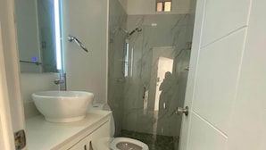 Un baño moderno con un tocador blanco, un espejo grande, un lavabo blanco, un inodoro y una zona de ducha con mampara de cristal.