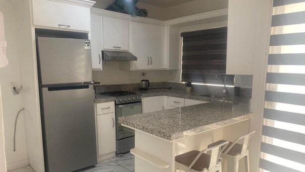 Una cocina con armarios blancos, un refrigerador de acero inoxidable, una estufa a gas y una encimera de granito.