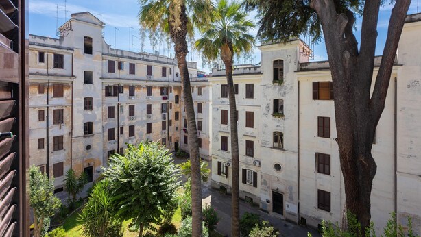 A courtyard with multi-story buildings, palm trees, and a view of the sky.