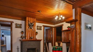 A cozy living room with a fireplace, wooden ceiling, and a dining area with chairs and a table. - Ap in Capivari - Tirol31 By Temporada Férias (Campos do Jordão)