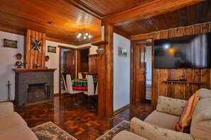 Una sala de estar acogedora con chimenea, paredes de madera, un televisor montado en la pared y un comedor con mesa y sillas.