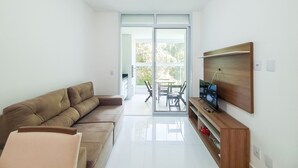 A modern living room with a sectional sofa, a flat-screen TV mounted on the wall, and a sliding glass door leading to an outdoor patio area.