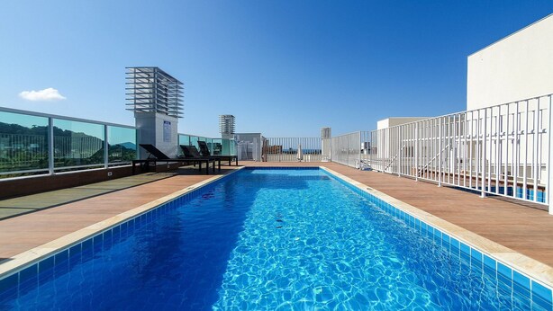 A rooftop swimming pool with clear blue water, surrounded by a wooden deck and white railings.