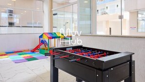 A foosball table and a colorful play area in a hotel lobby with large windows and a view of the building's interior.