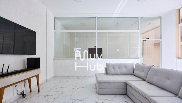 A modern living room with a large flat-screen TV, a grey sectional sofa, and a marble floor.