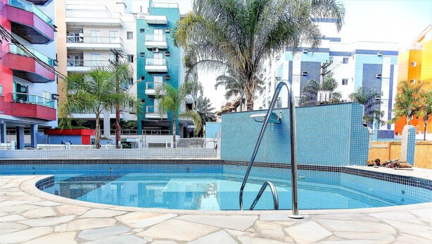 Una piscina con solarium de piedra, rodeada de edificios de varios pisos con balcones y palmeras.