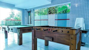 Una mesa de billar en una habitación con paredes de azulejos y vistas al exterior con vegetación.