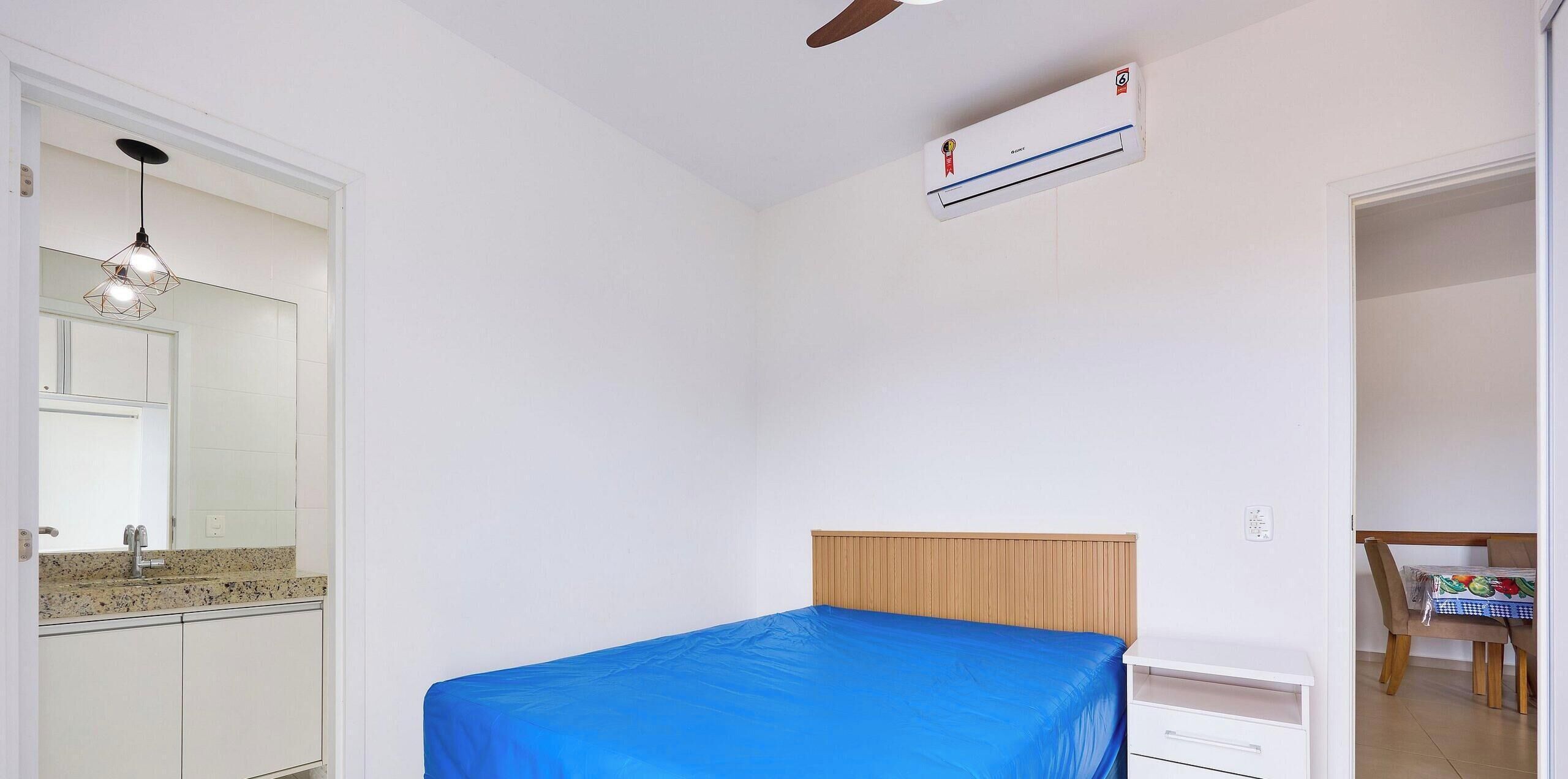 Un dormitorio con cama, mesita de noche, escritorio, silla, ventilador de techo y aire acondicionado.