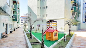 A children's play area with a slide, swings, and a small house structure. - Apartment at Big Beach TF305 By Temporada Férias (Ubatuba)
