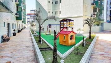 Espaço infantil com escorrega, baloiços e uma casinha.