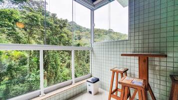 Uma varanda com vista para vegetação exuberante, uma parede revestida de azulejos e uma pequena mesa de madeira com bancos.