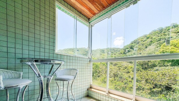 Ein Balkon mit Blick auf einen grünen Hang, einem Glastisch und zwei Korbstühlen.