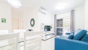 Ein modernes Wohnzimmer mit einem blauen Sofa, einem weißen Esstisch und einem Fernseher.