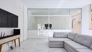 A modern living room with a large flat-screen TV, a grey sectional sofa, and a marble floor. - New apartment with air conditioning - REF JS45H (Ubatuba)