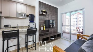 A modern kitchen with a microwave, a flat-screen TV, and a dining area with two bar stools. - New apartment with air conditioning - REF JS45H (Ubatuba)