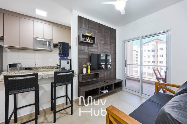 A modern kitchen with a microwave, a flat-screen TV, and a dining area with two bar stools.