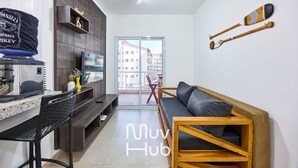A modern living room with a sofa, a wooden coffee table, a TV, and a dining area with a bench and a small table. - New apartment with air conditioning - REF JS45H (Ubatuba)