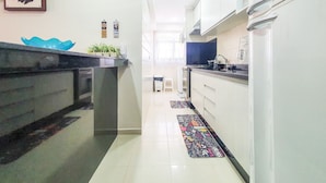 A modern kitchen with white cabinets, a black countertop, and a blue decorative bowl. There are potted plants on the counter and a colorful rug on the floor. - Penthouse with Private Pool - REF 0150 (Ubatuba)