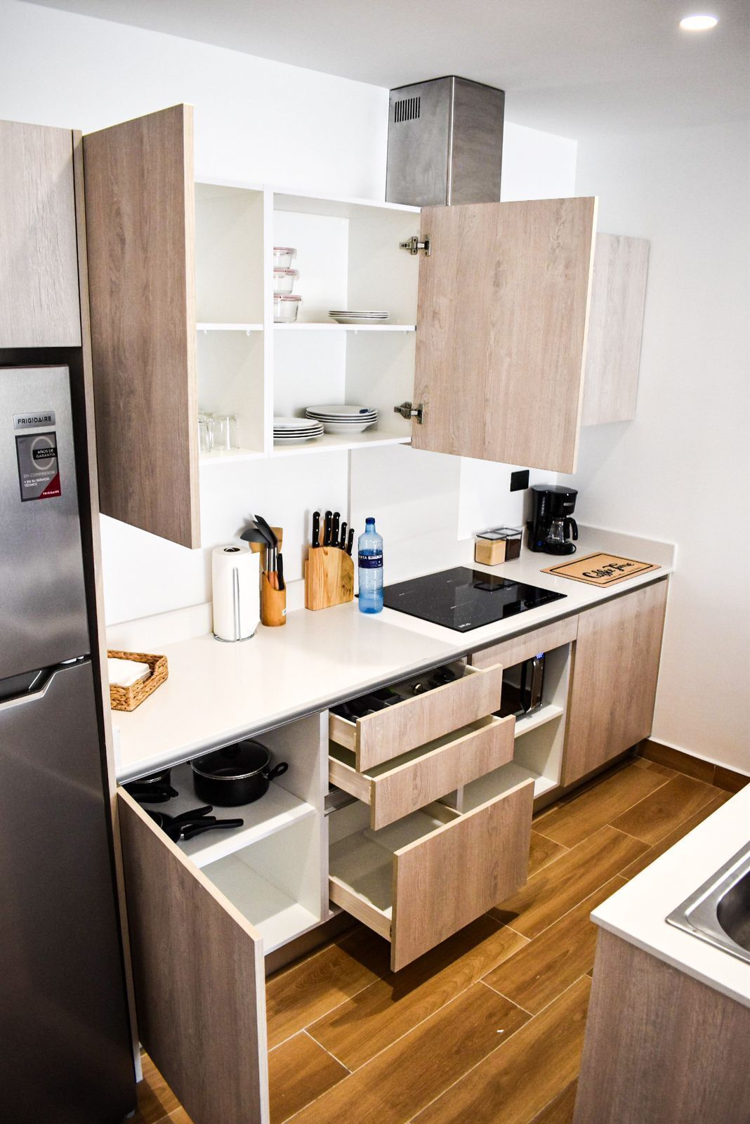 A modern kitchen with a built-in refrigerator, wooden cabinets, a black induction cooktop, and a coffee maker.