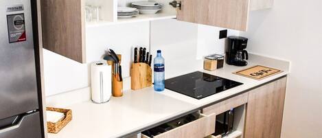 A modern kitchen with a built-in refrigerator, wooden cabinets, a black induction cooktop, and a coffee maker.