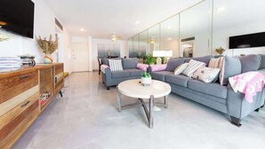 Ein modernes Wohnzimmer mit einem grauen Sofa, einer Holzkommode, einem runden Couchtisch und einem großen Spiegel.