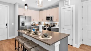 A modern kitchen with stainless steel appliances, a central island with stools, and pendant lighting. - Cozy Comfort1bd Attached Garage+Desk+Pool+Gym (Fort Worth)