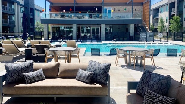 A rooftop pool area with lounge chairs and a sofa, a pool, and a building with a balcony in the background. - Cozy Comfort1bd Attached Garage+Desk+Pool+Gym (Fort Worth)